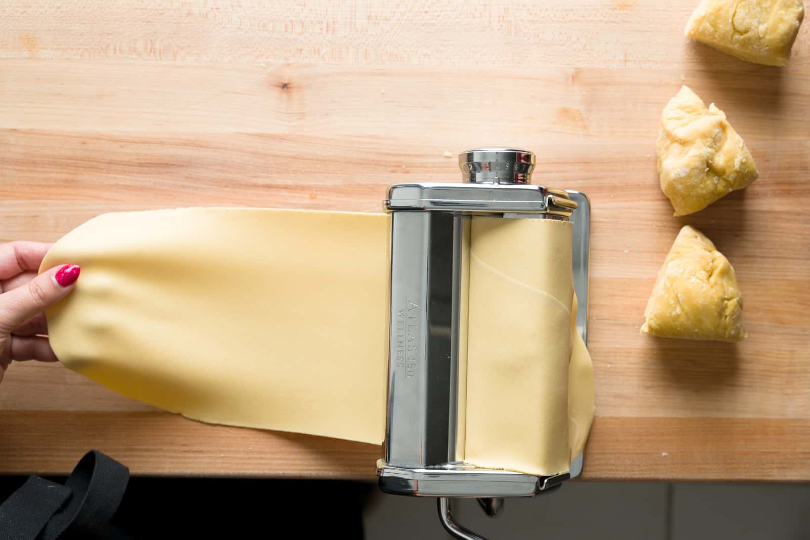 Fresh pasta flattened by a pasta machine next to three pasta dough balls