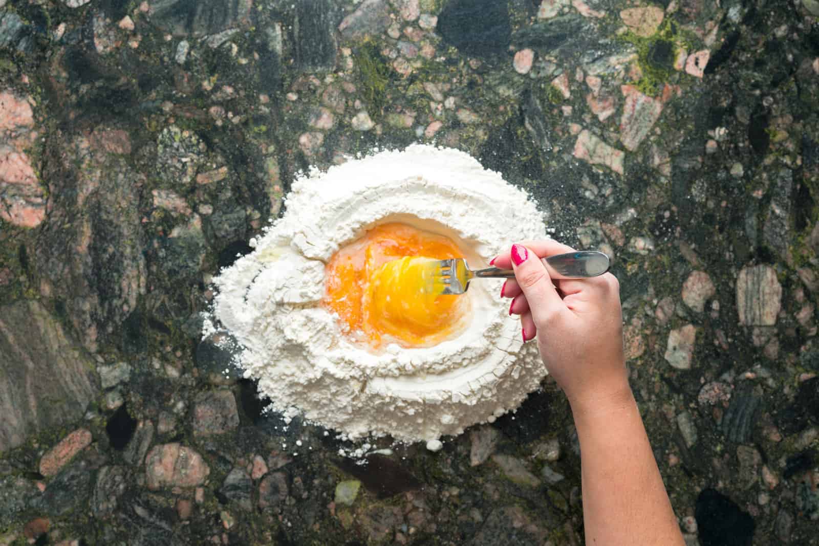 Four eggs being stirred inside a flour well being for fresh pasta