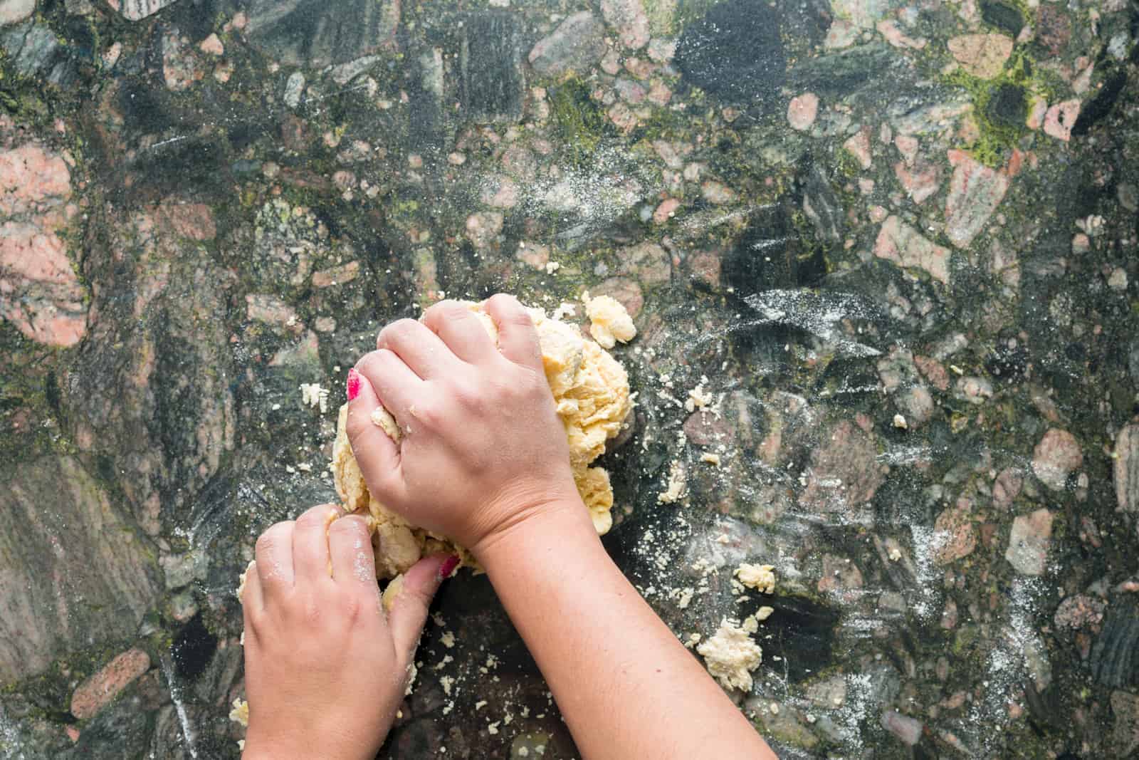Two hands kneading fresh pasta dough on a kitchen countertop