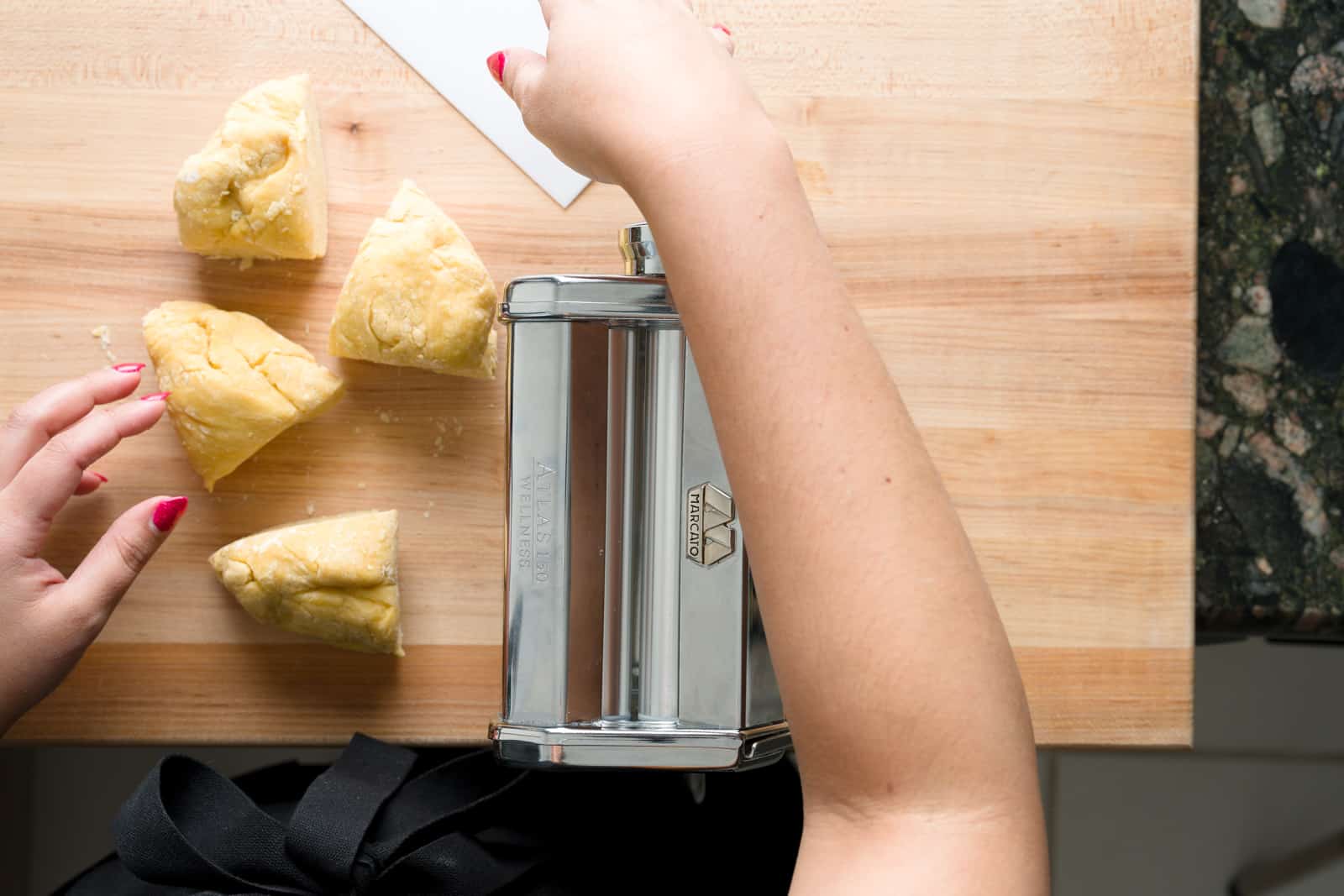 Four fresh pasta dough balls on a kitchen board before being flattened by a pasta machine