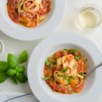 Fresh tomato pasta sauce - Two plates of pasta tossed in fresh tomato sauce in a scene with fresh basil, cherry tomatoes, beverage and cloth napkin