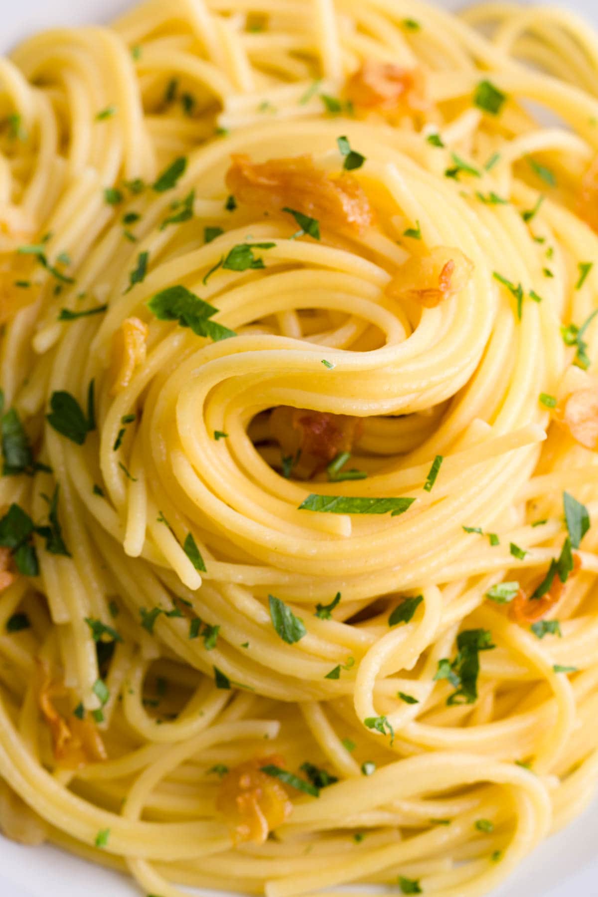 Close up shot of aglio e olio spaghetti with pieces of garlic and chopped parsley.