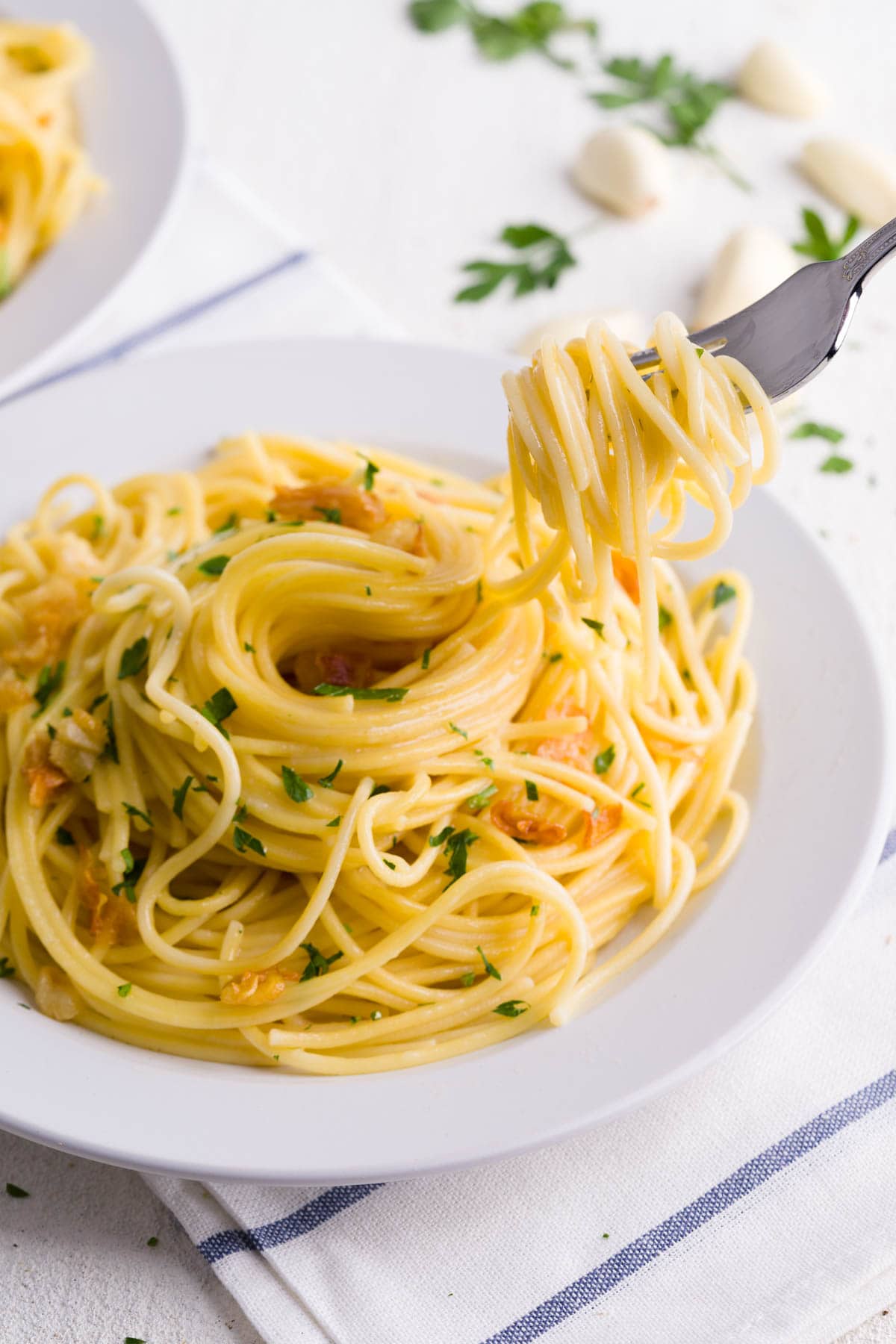 Aglio e olio pasta on a plate served with parsley and twirled on a fork.
