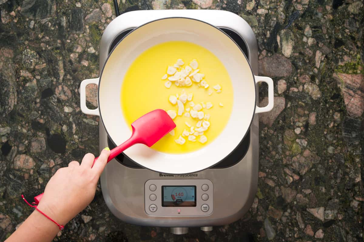 Shallow frying garlic chips in olive oil on a pan on top of hot plate.
