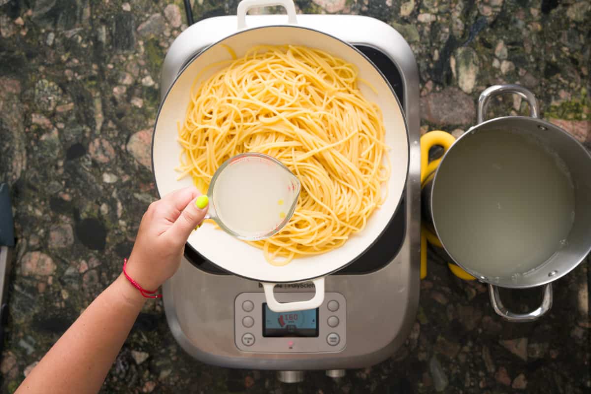 Adding pasta water to the pan with the spaghetti aglio e olio.
