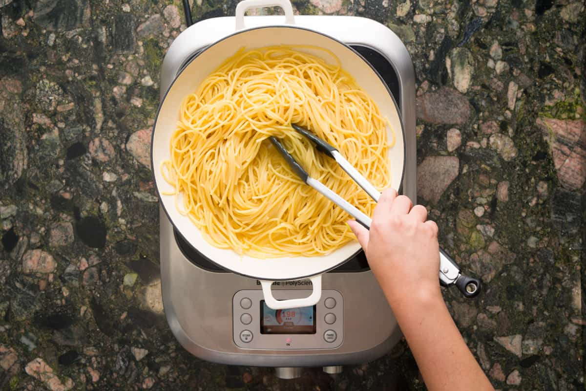 Mixing the pasta, olive oil and and pasta water together in a pan on top of a hot plate.