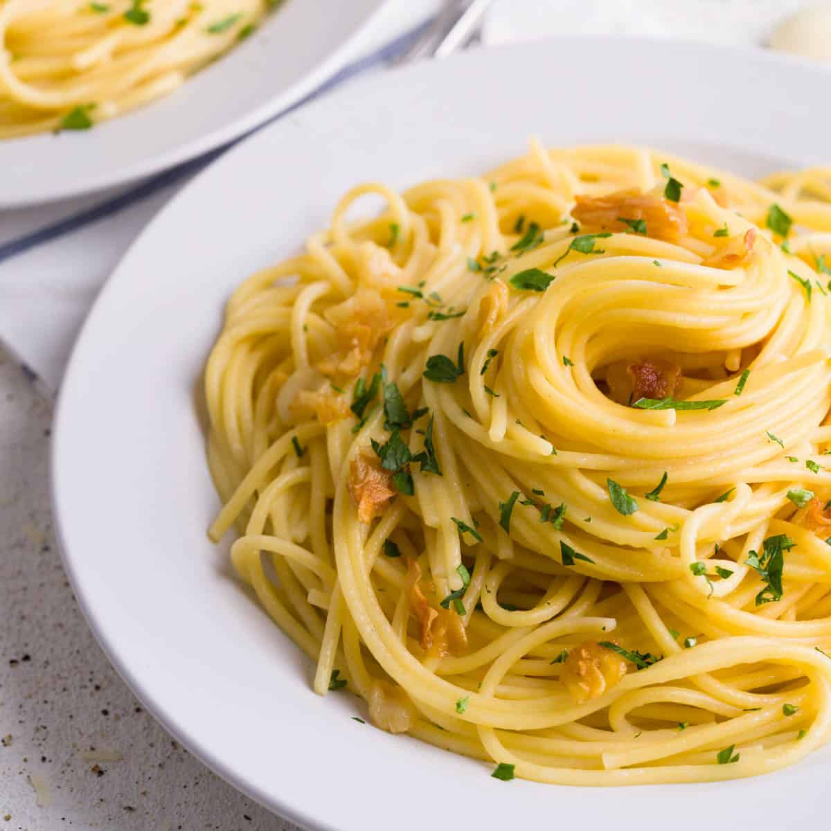 Plate of spaghetti aglio e olio topped with golden garlic slices and chopped parsley on a white dish