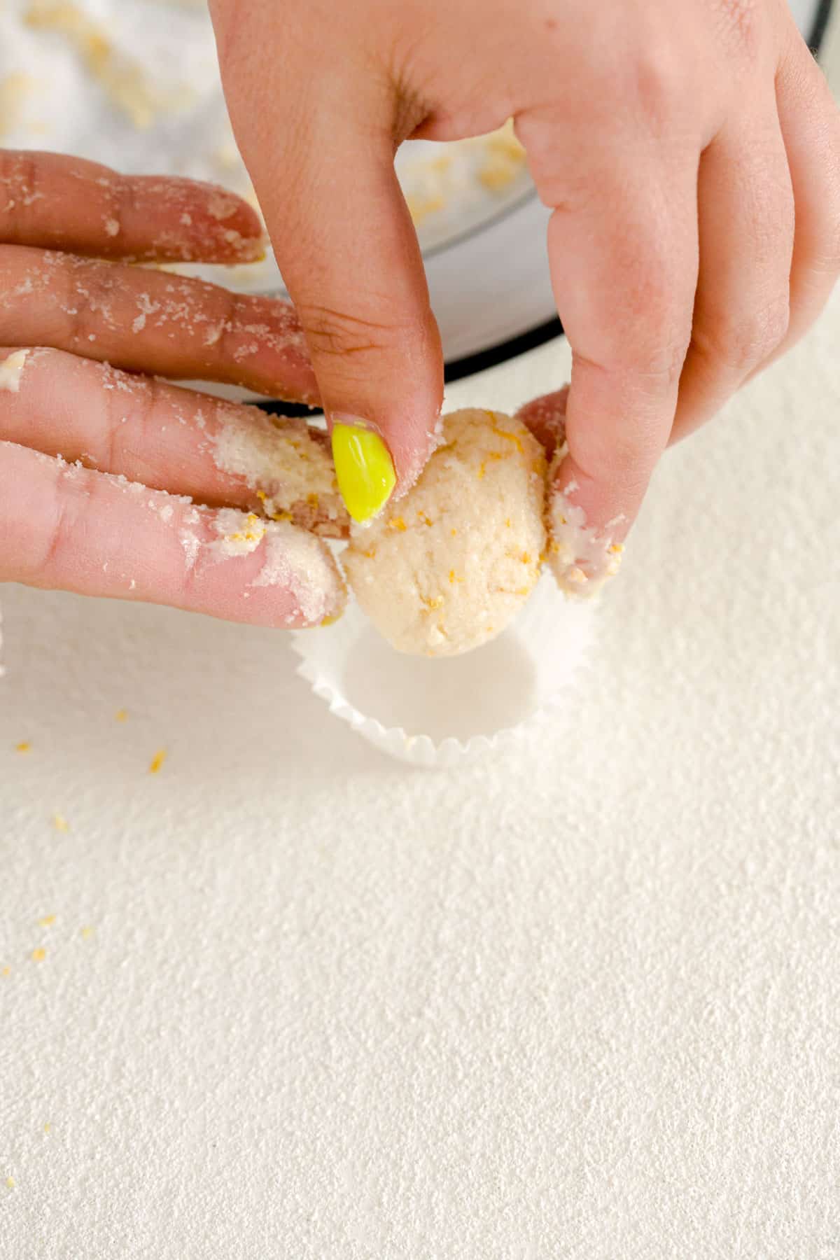 Placing lemon truffles in a mini baking cup on a white background.