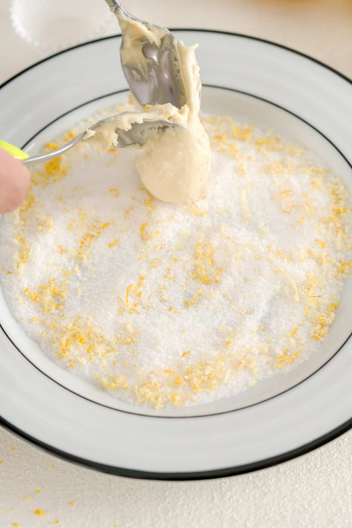Placing lemon truffles in granulated sugar and lemon zest coating on a white and black dish.