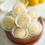 Lemon truffles stacked on a plating dish next to cut and whole lemons.