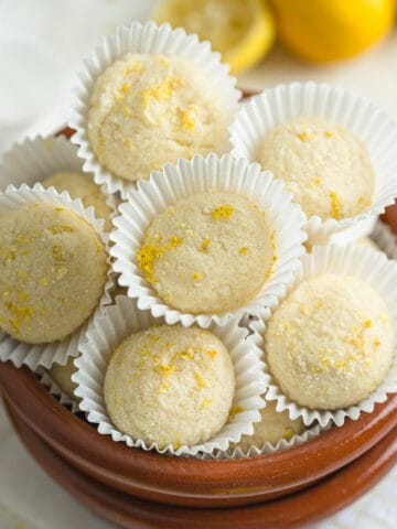 Lemon truffles stacked on a plating dish next to cut and whole lemons.