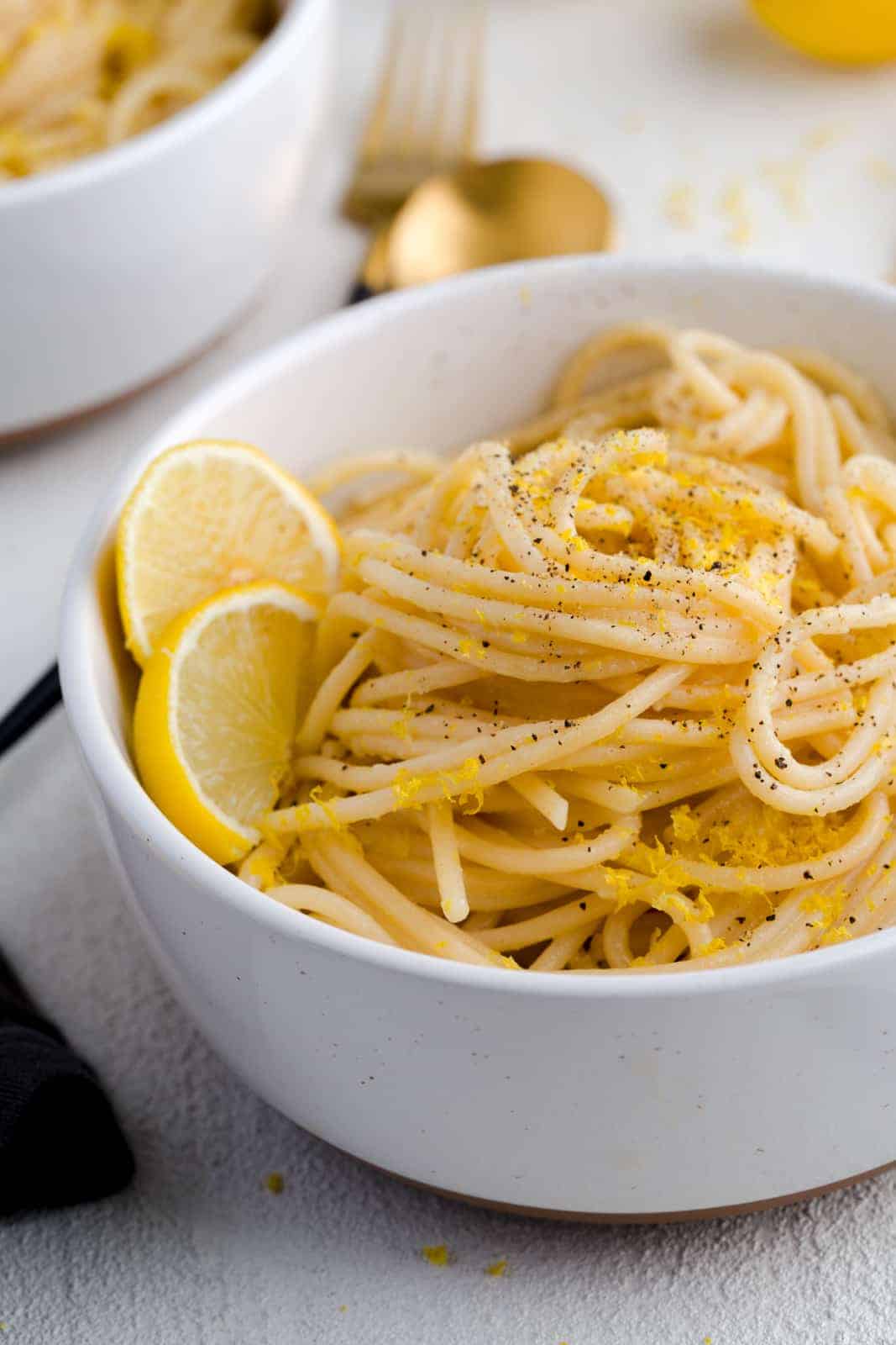 Pasta al limone in a bowl, garnished with freshly cracked pepper and two lemon slices.
