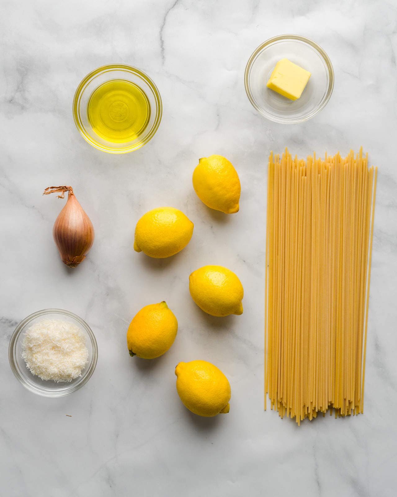 Ingredients for pasta al limone shown on a marble countertop - parmesan cheese, lemons, shallots, butter, extra virgin olive oil, spaghetti