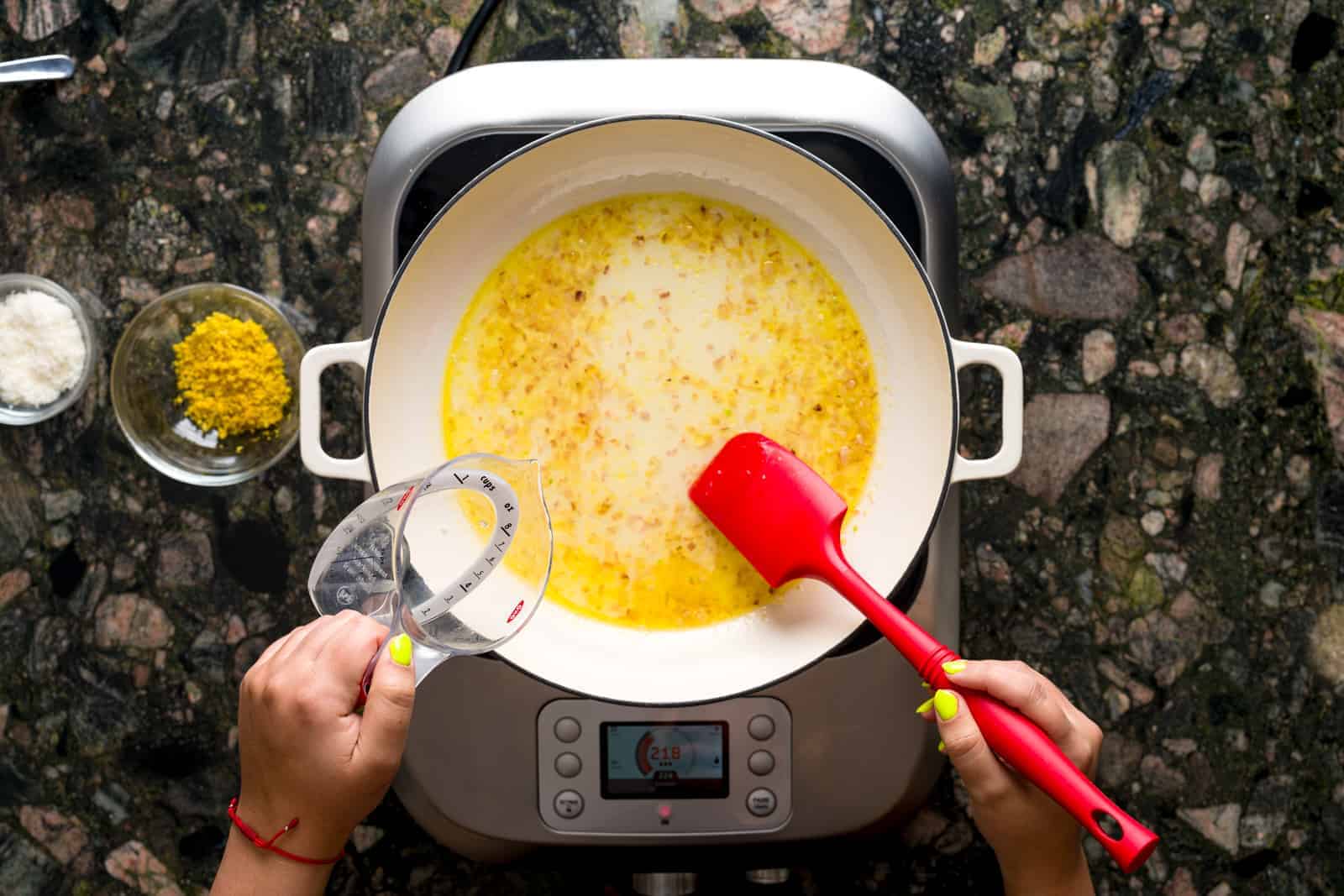 Pasta al limone - Pan showing sautéed shallots in olive oil and butter using a red spatula. Pasta water is also being poured into the pan.