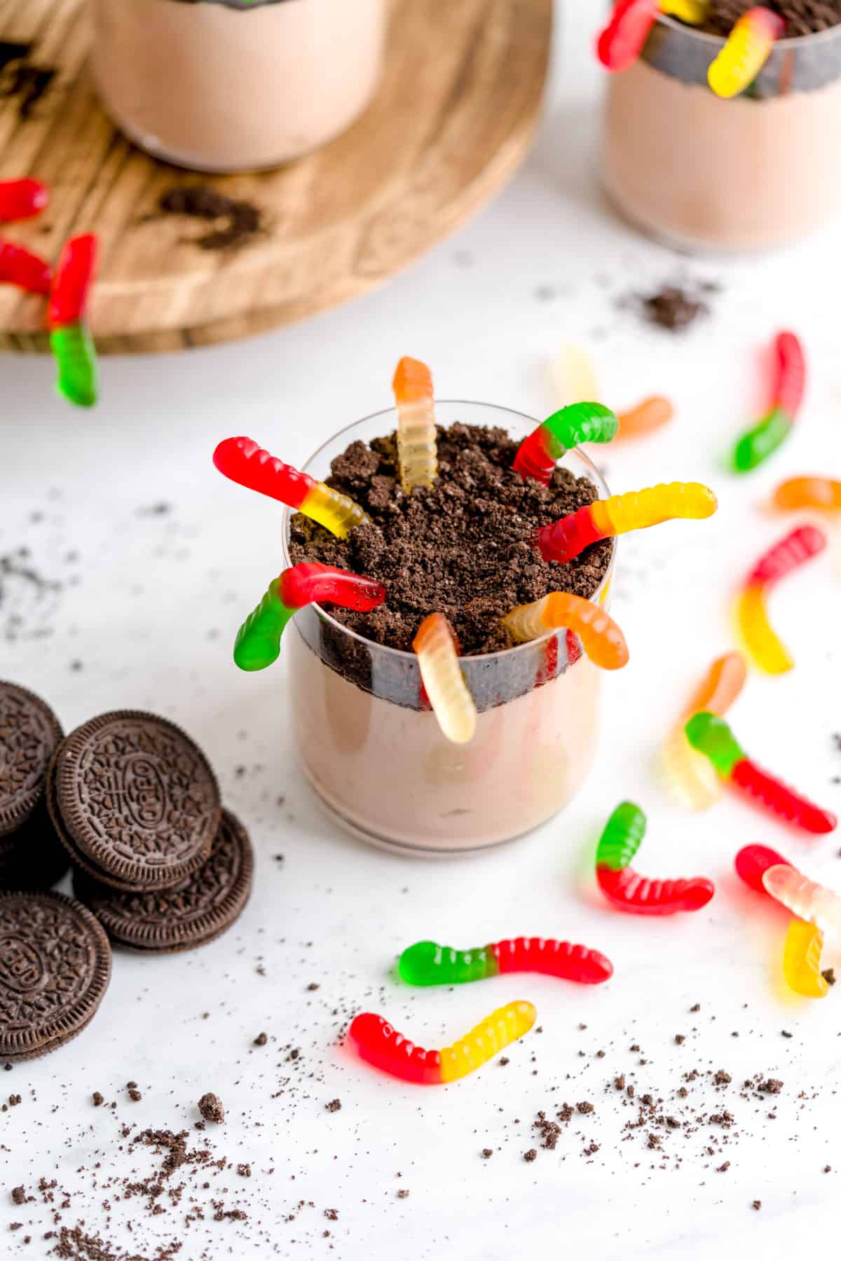 4 ingredient easy dirt cup shown with gummy worms at the top surrounded by Oreos, cookie crumbs and gummy worms.