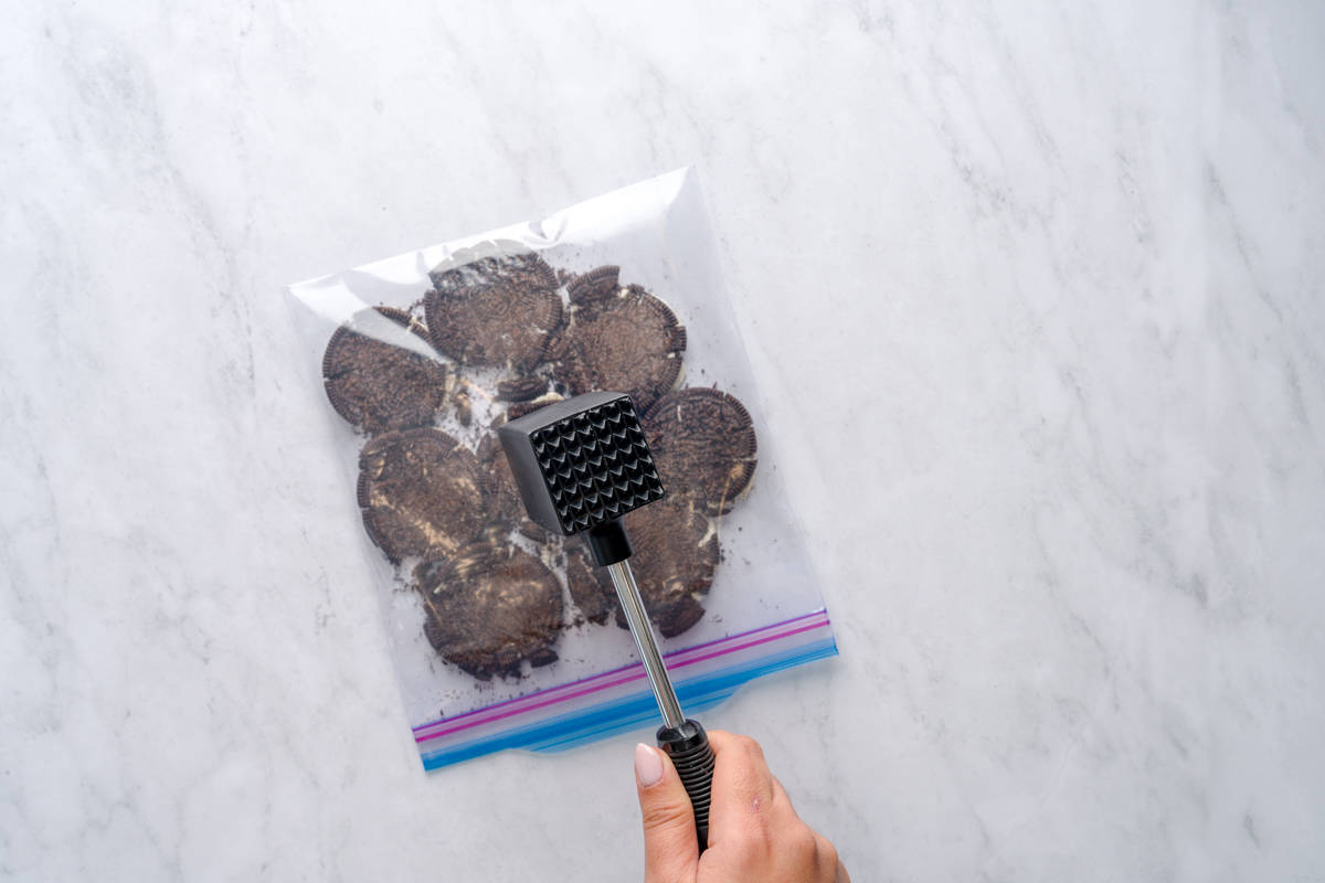 Crushing Oreo cookies with meat tenderizer to make kids dirt cups.