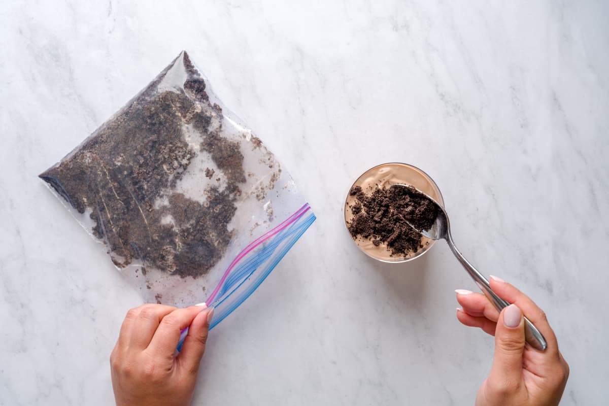 Spooning crushed Oreos on glass full of Nutella yogurt for kids dirt cup recipe.