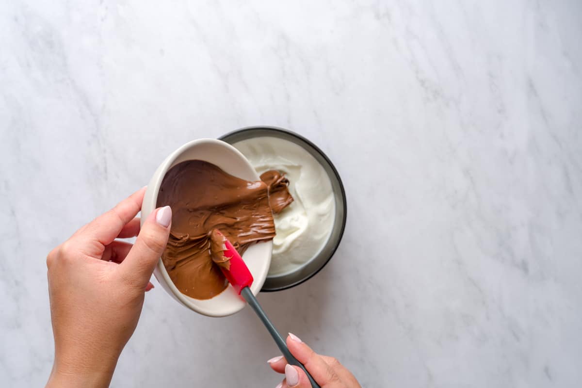 Pouring Nutella into a bowl of Greek yogurt.