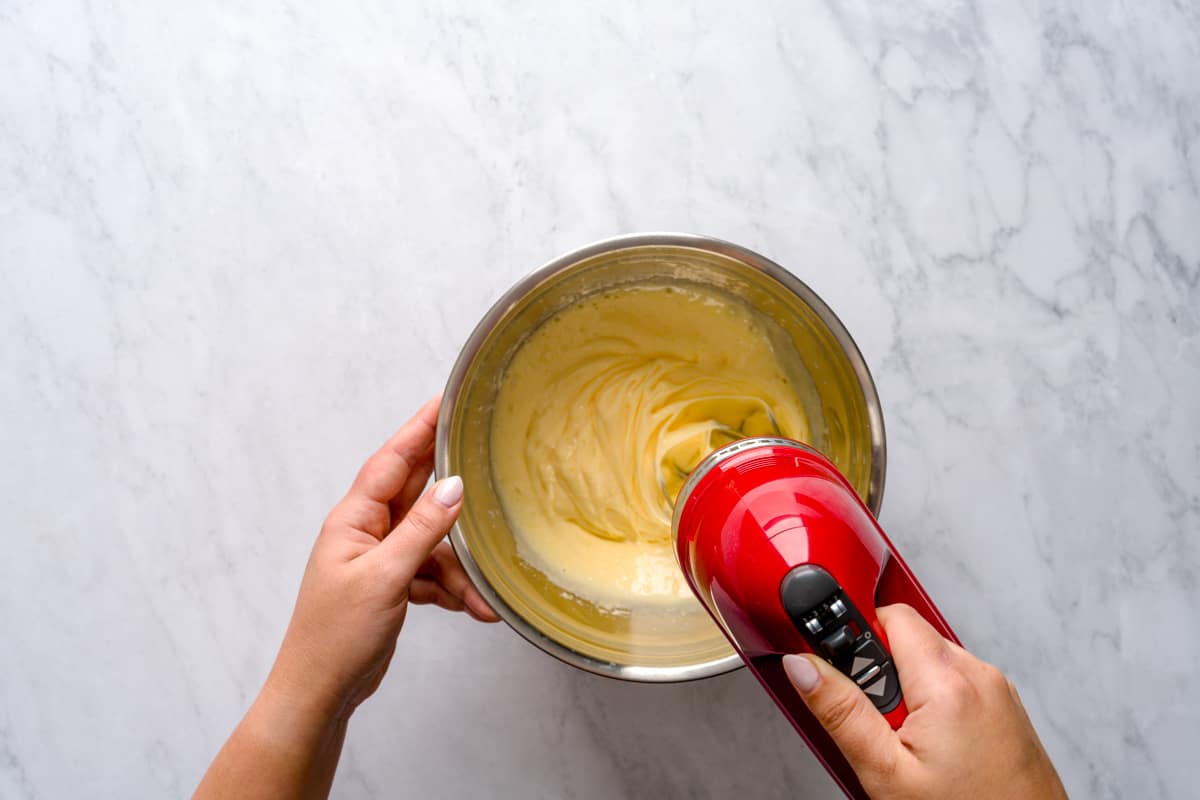 Beating the eggs and granulated sugar on a metal bowl using a handheld mixer.