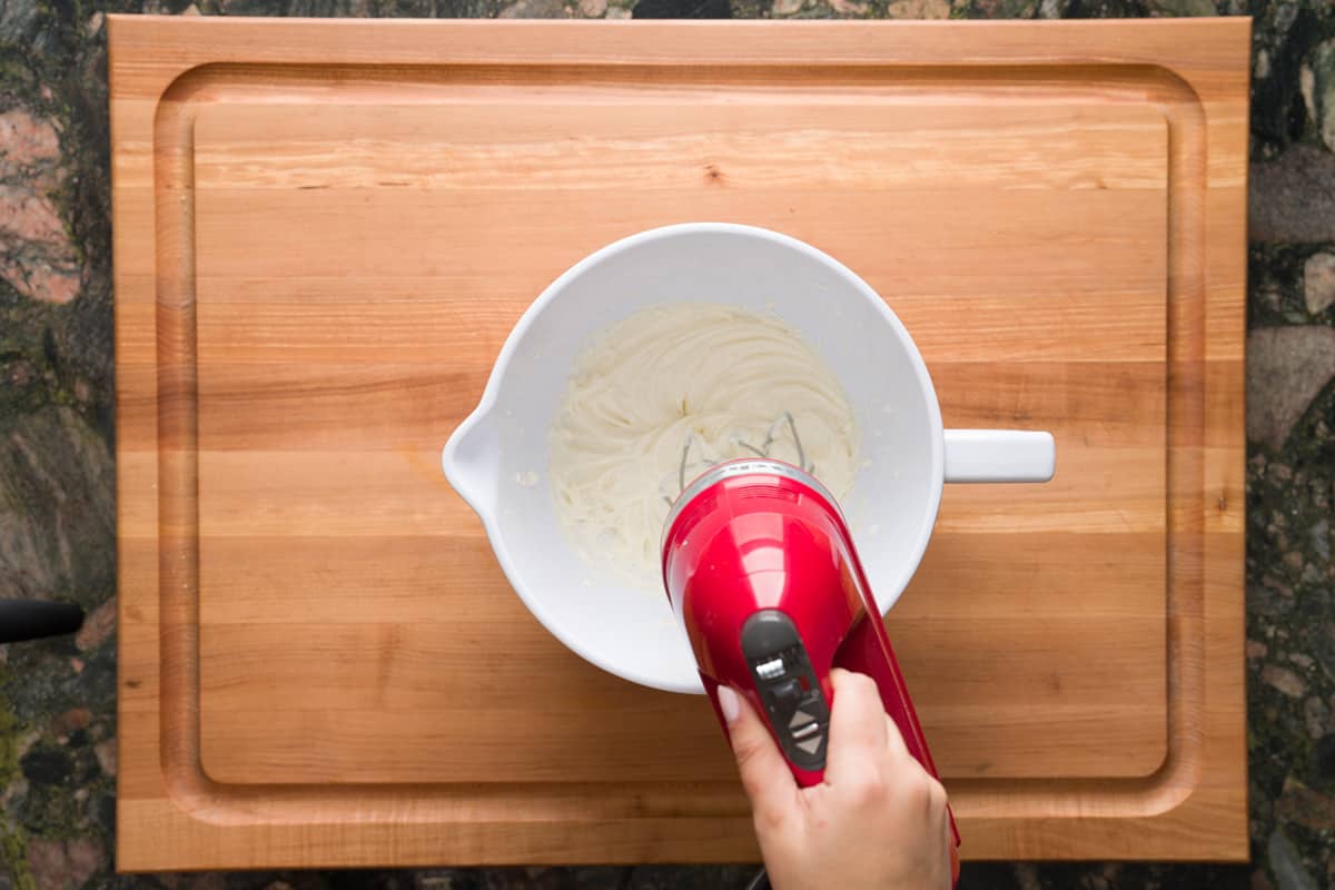 Beating ingredients for the mascarpone frosting using a handheld mixer.