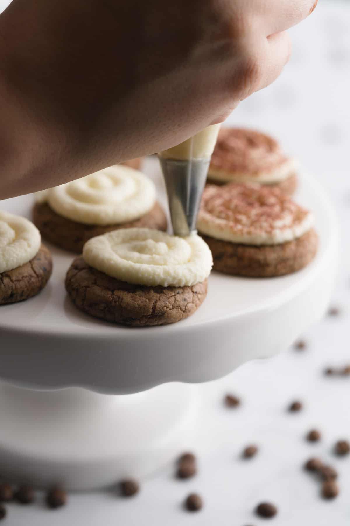 Piping mascarpone cream frosting on top of coffee chocolate tiramisu cookies.