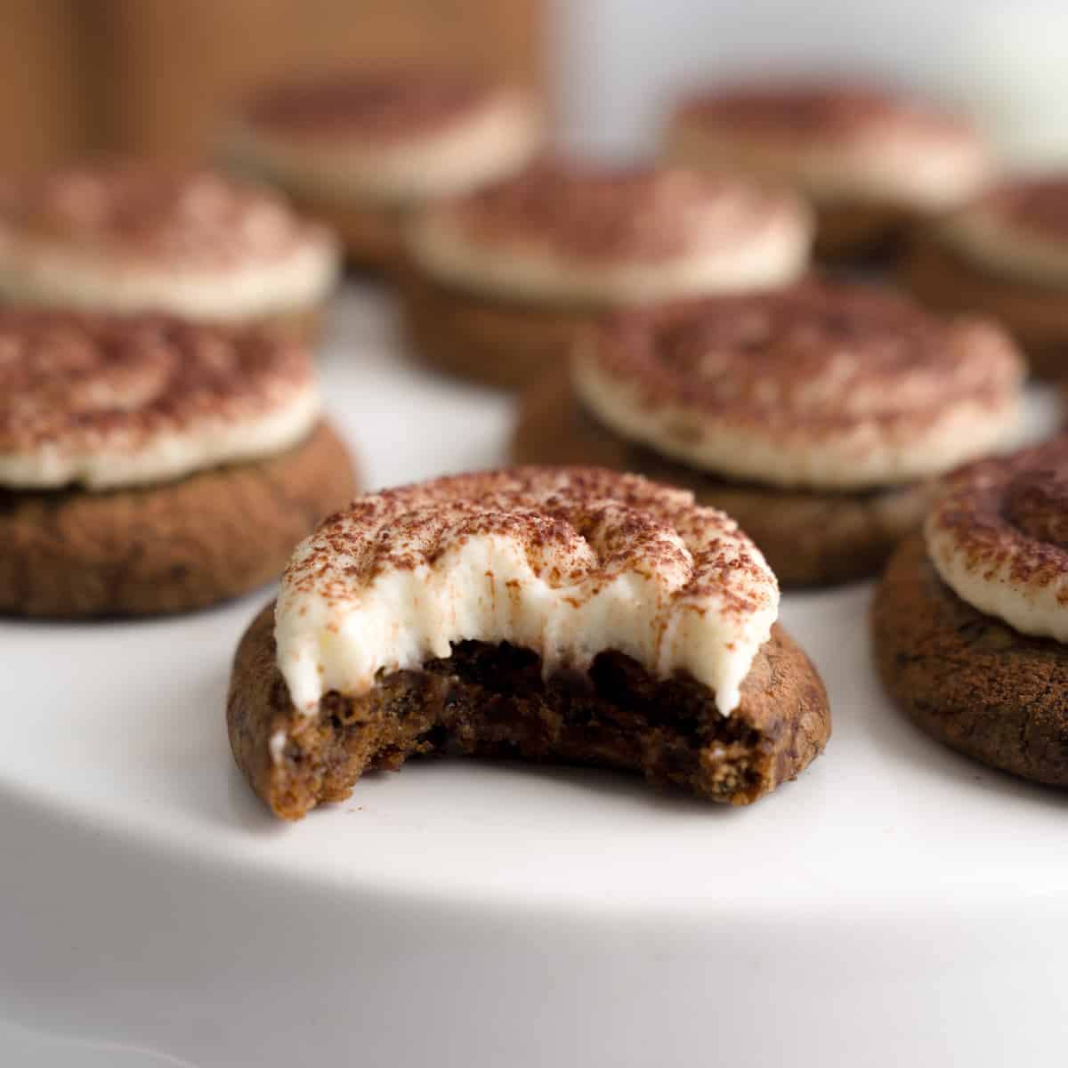 Close-up of a tiramisu cookie with a bite taken out, topped with mascarpone frosting and cocoa.