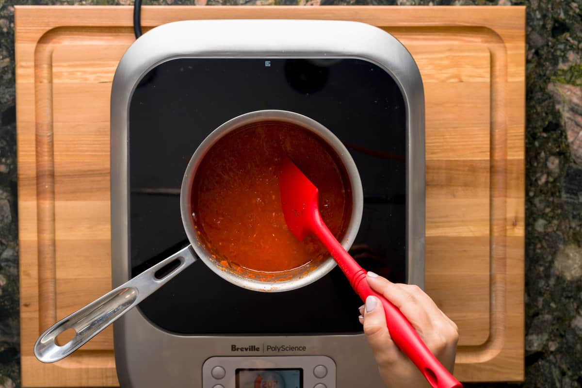 A red spatula stirring a pizza sauce-filled pot simmering on a stove.
