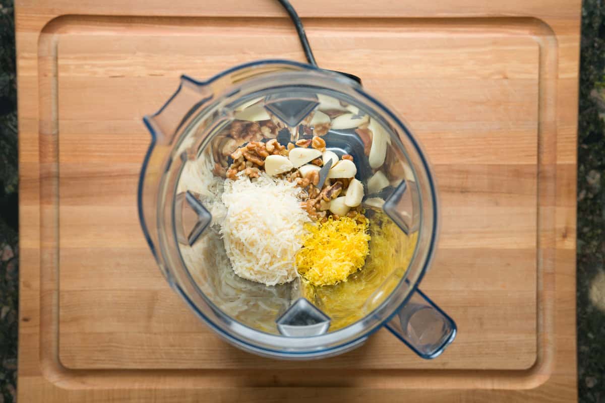 Blender about to blend lemon basil pesto. Inside are garlic cloves, parmesan cheese, walnuts and lemon zest.