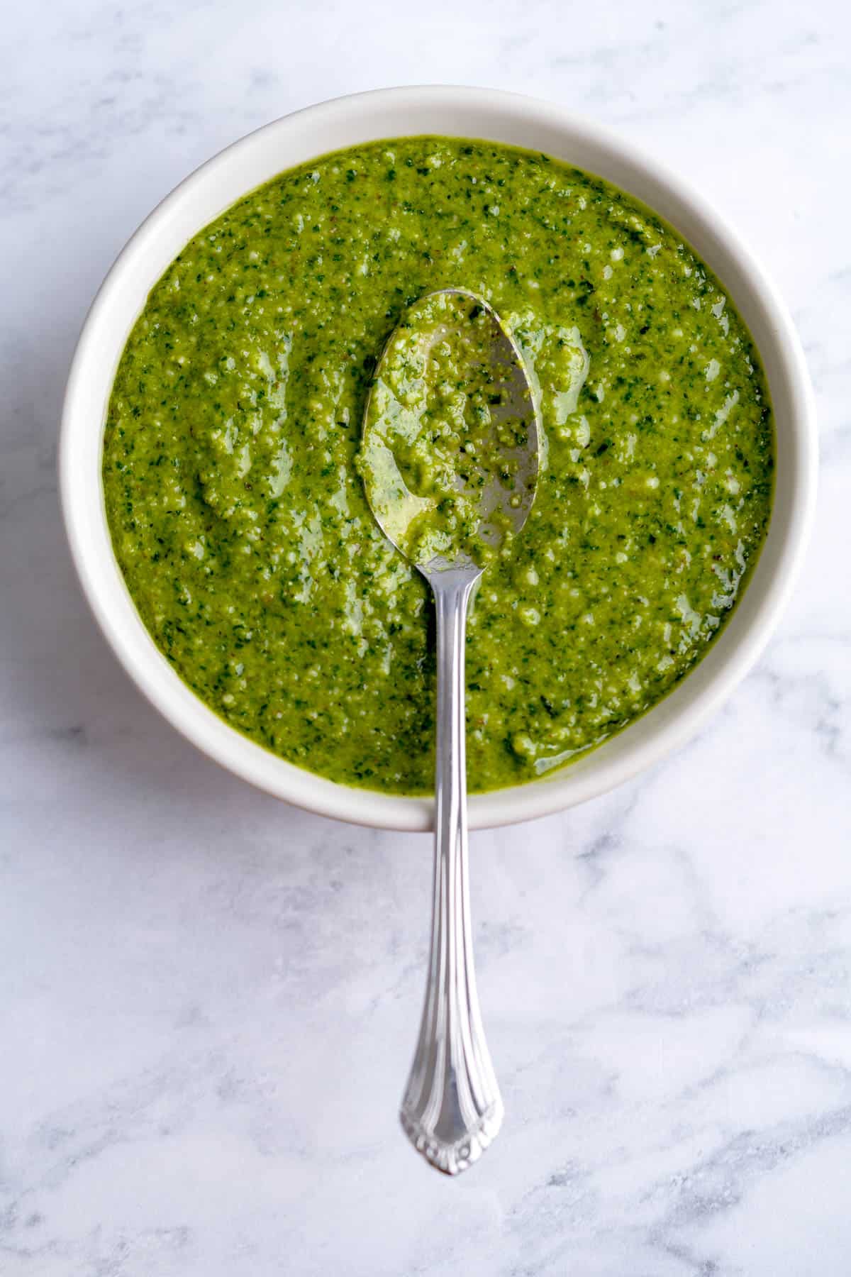 A bowl full of lemon basil pesto with a spoon on top, showing the consistency of the pesto sauce.