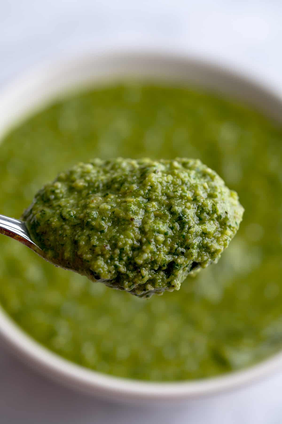 A spoon showing the consistency of lemon basil pesto.