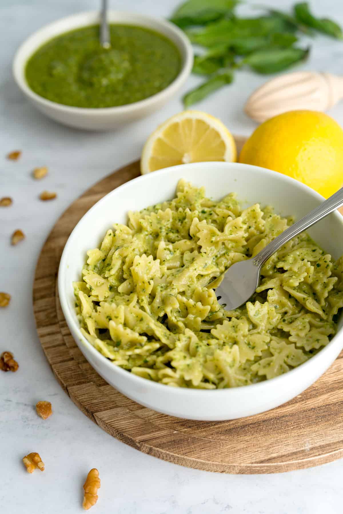 Bowtie farfale pasta with basil pesto surrounded by lemons, walnuts, basil, pesto and a lemon juicer.