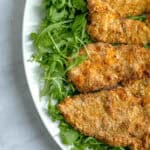 Air frier chicken cutlets arranged on a platter on top of fresh arugula.