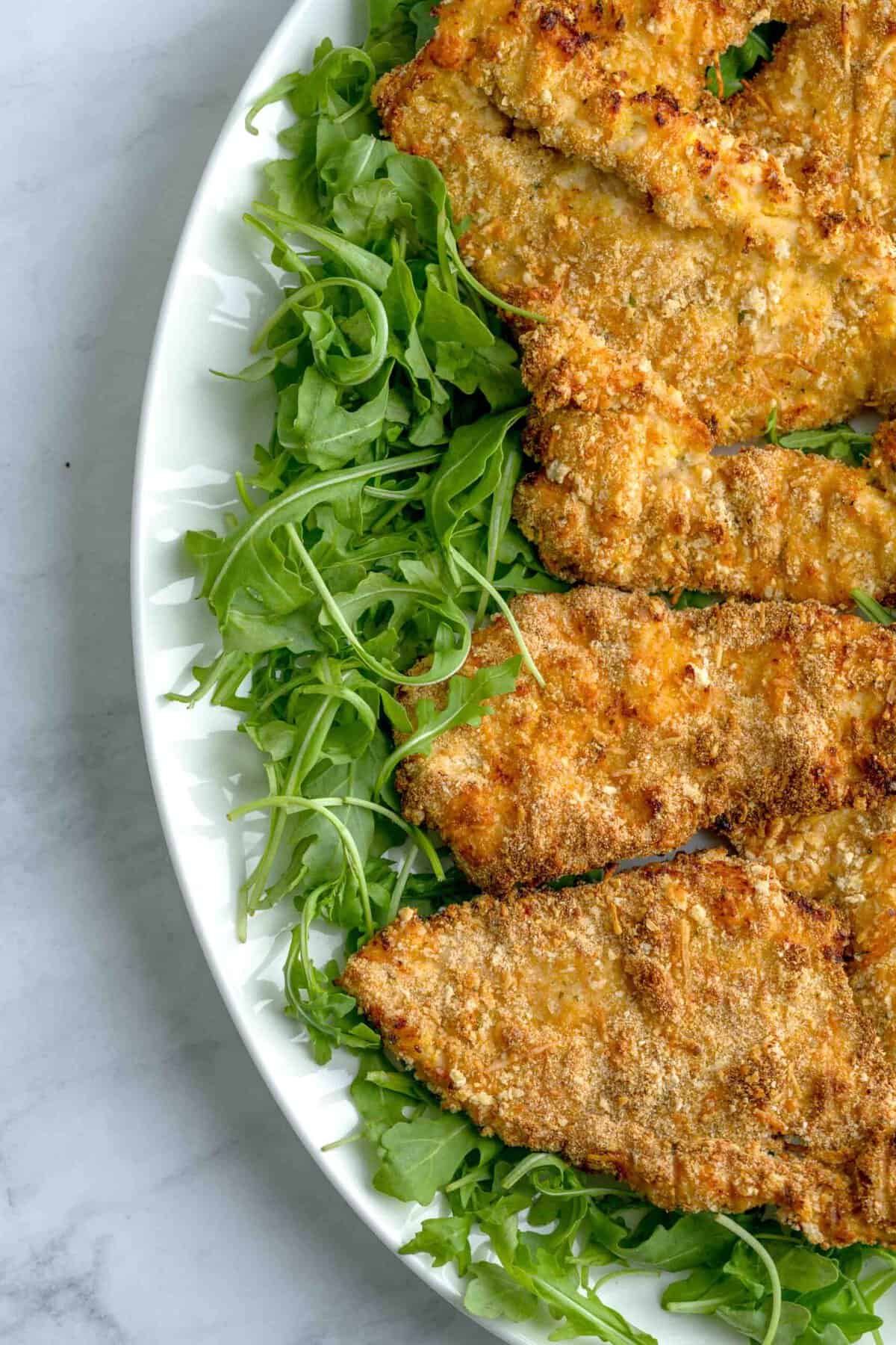 Air frier chicken cutlets arranged on a platter on top of fresh arugula.