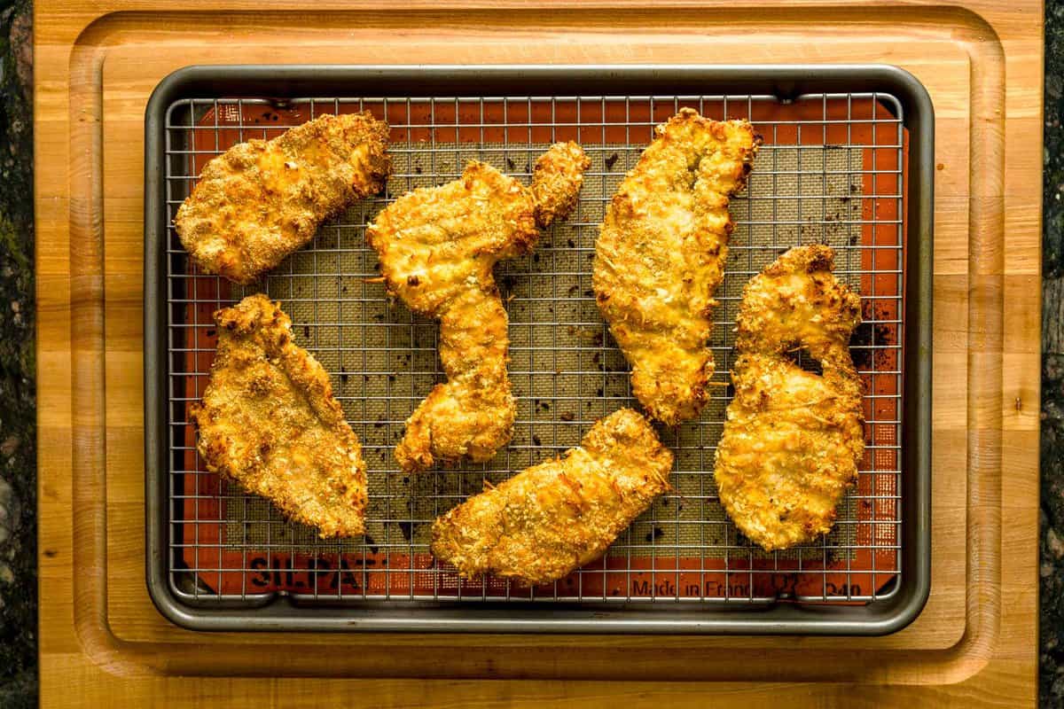 Breaded, air fryer chicken cutlets on top of a wire rack on top of a baking sheet.