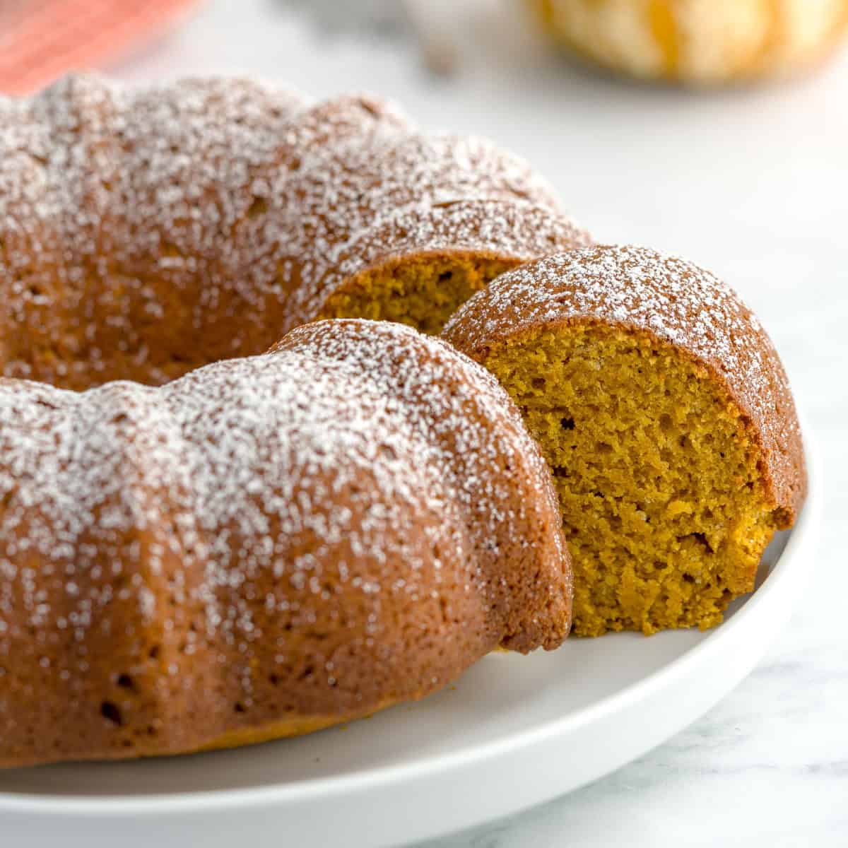 Close-up of a sliced pumpkin spice bundt cake topped with powdered sugar on a white plate.