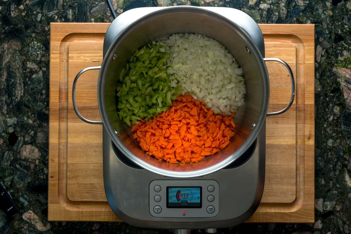 A top-down shot of a large pot over an induction burner. Inside the pot is diced celery, onions and carrots.
