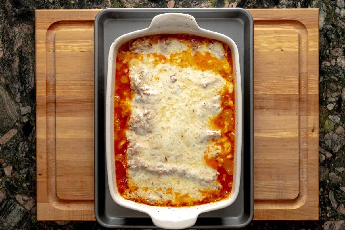Lasagna pan just out of the oven, filled with a melty cheese lasagna bolognese, above a baking sheet.