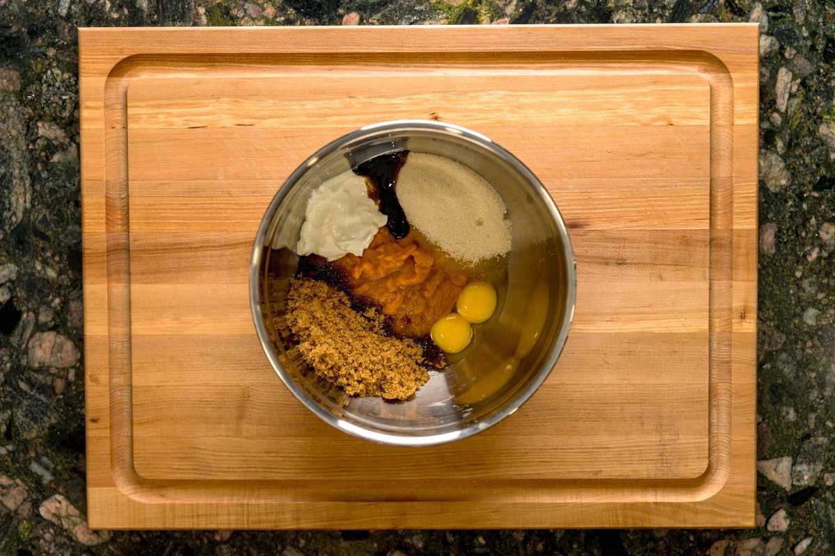 A metal bowl holding the wet ingredients for a pumpkin pie spice cake, including: pumpkin puree, granulated sugar, brown sugar, egg yolks, sour cream and vanilla bean paste.