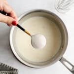 Overhead shot of shallot béchamel in a pot with the back of a spoon showing the thickness of the sauce.