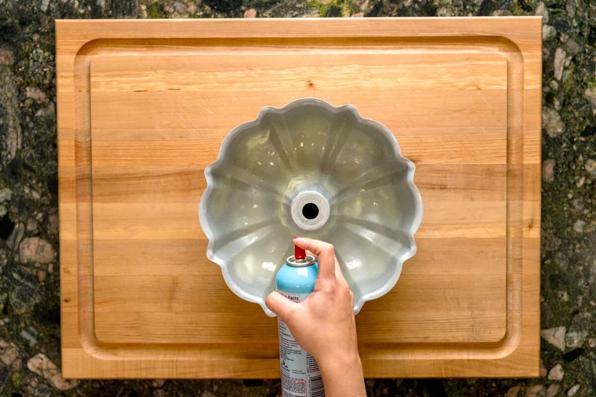 A hand spraying a Bundt pan with baking spray.