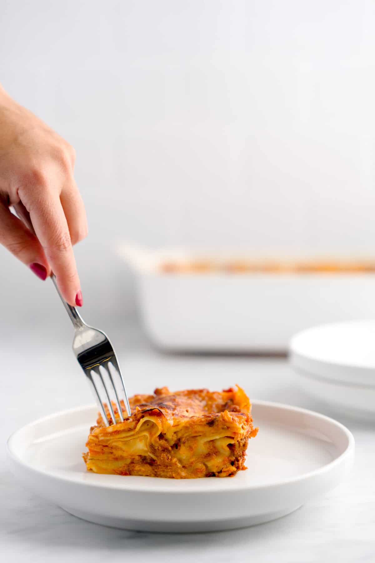 A portion of lasagna bolognese on a plate with a fork digging into it.