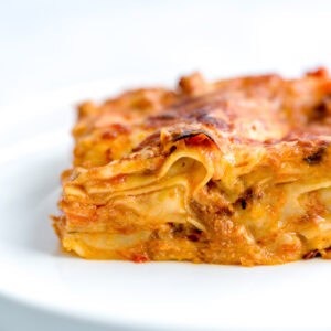 Close up shot of a lasagna piece, showing layers of béchamel sauce, bolognese sauce and cheese.