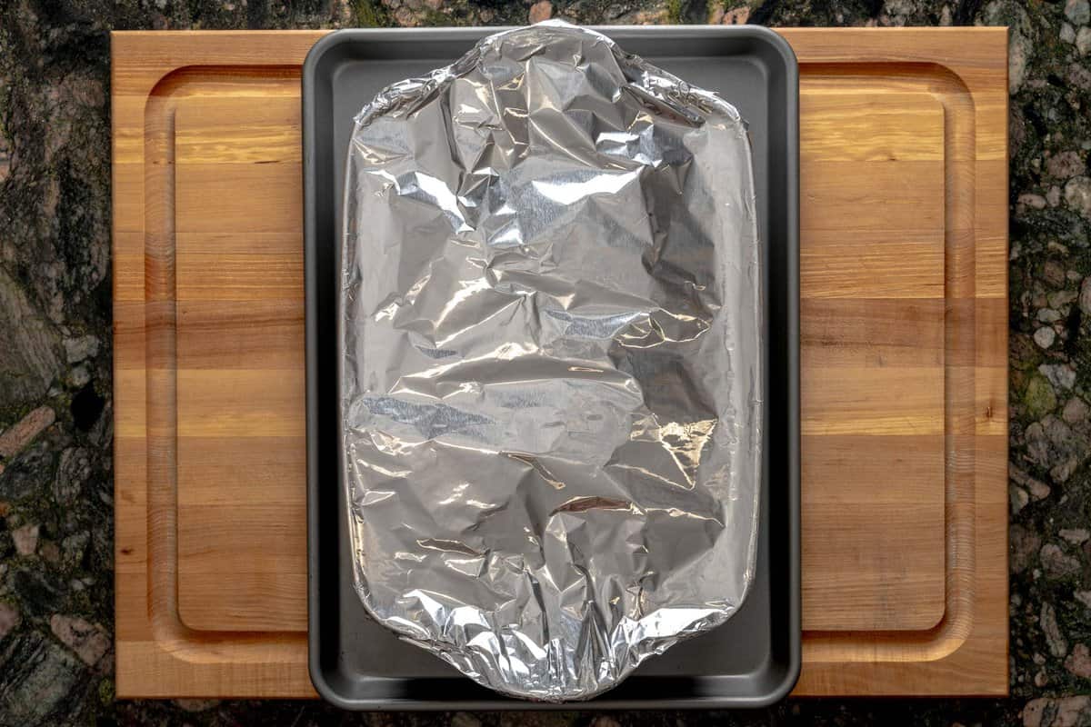 Lasagna pan covered with aluminum foil above a baking sheet.