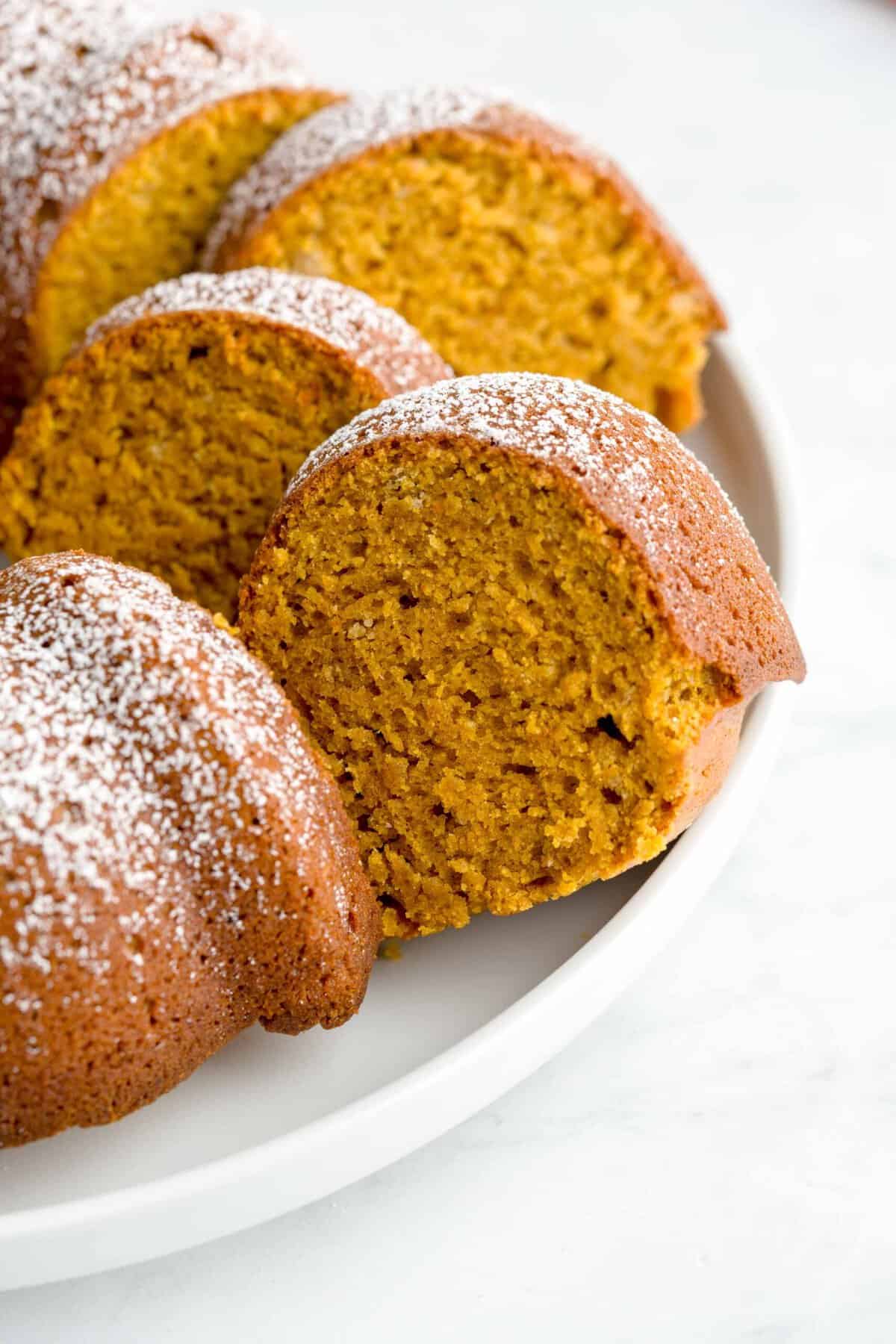 A close up shot of several pumpkin spice cake slices arranged next to the whole Bundt cake.
