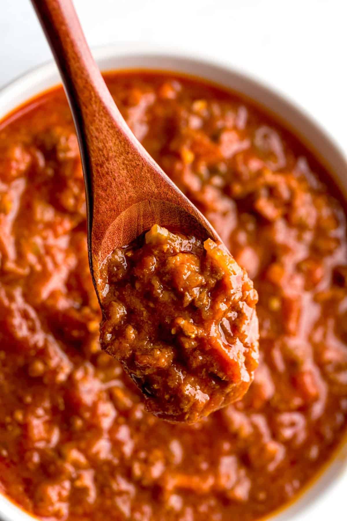 A wooden spoon filled with bolognese sauce over a bowl of bolognese sauce.