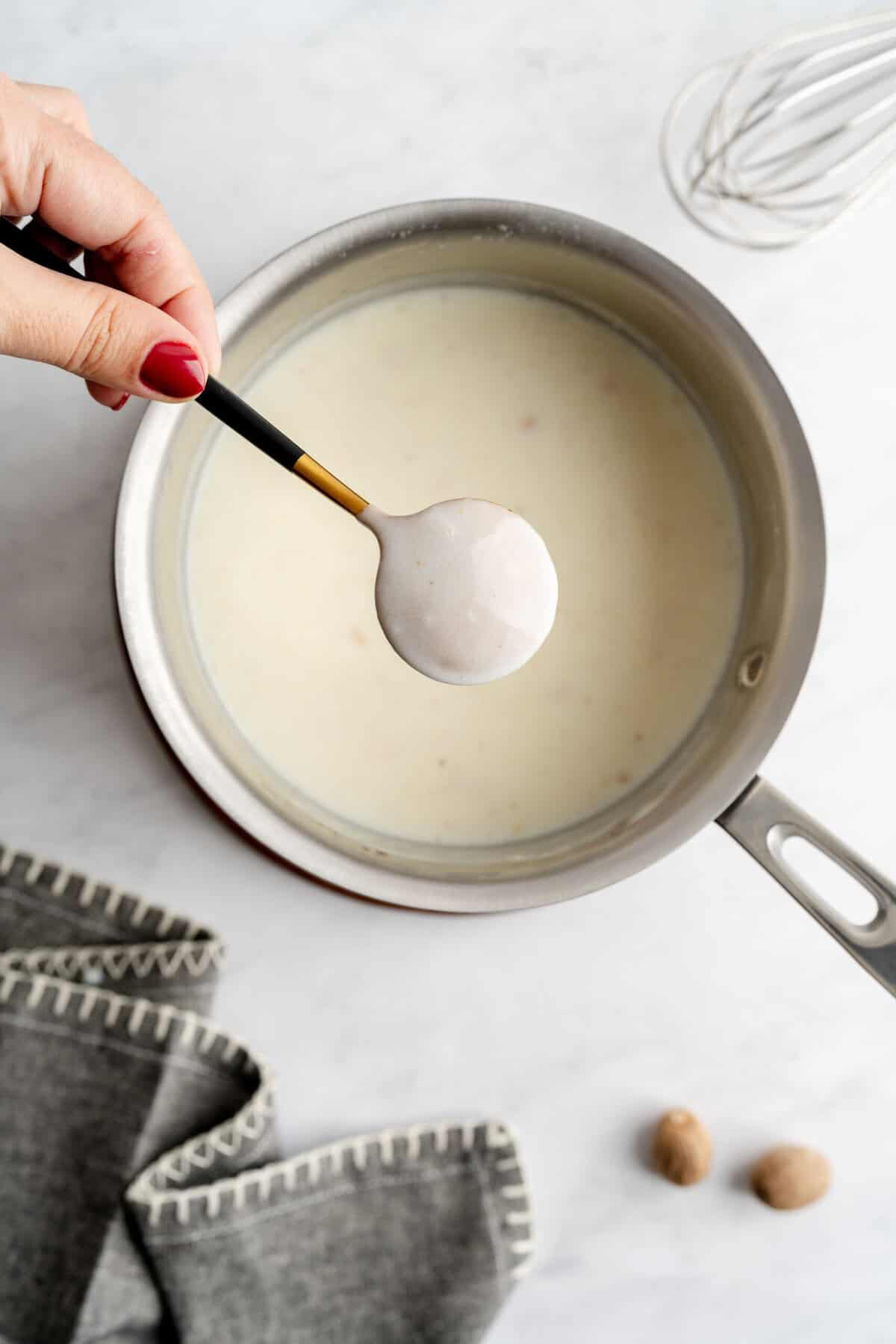 Overhead shot of shallot béchamel in a pot with the back of a spoon showing the thickness of the sauce.