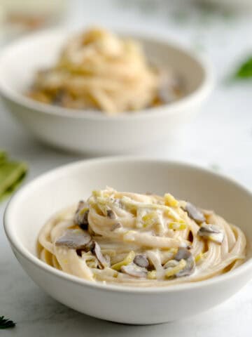 Two bowls of creamy leek and mushroom pasta next to a green cloth napkin