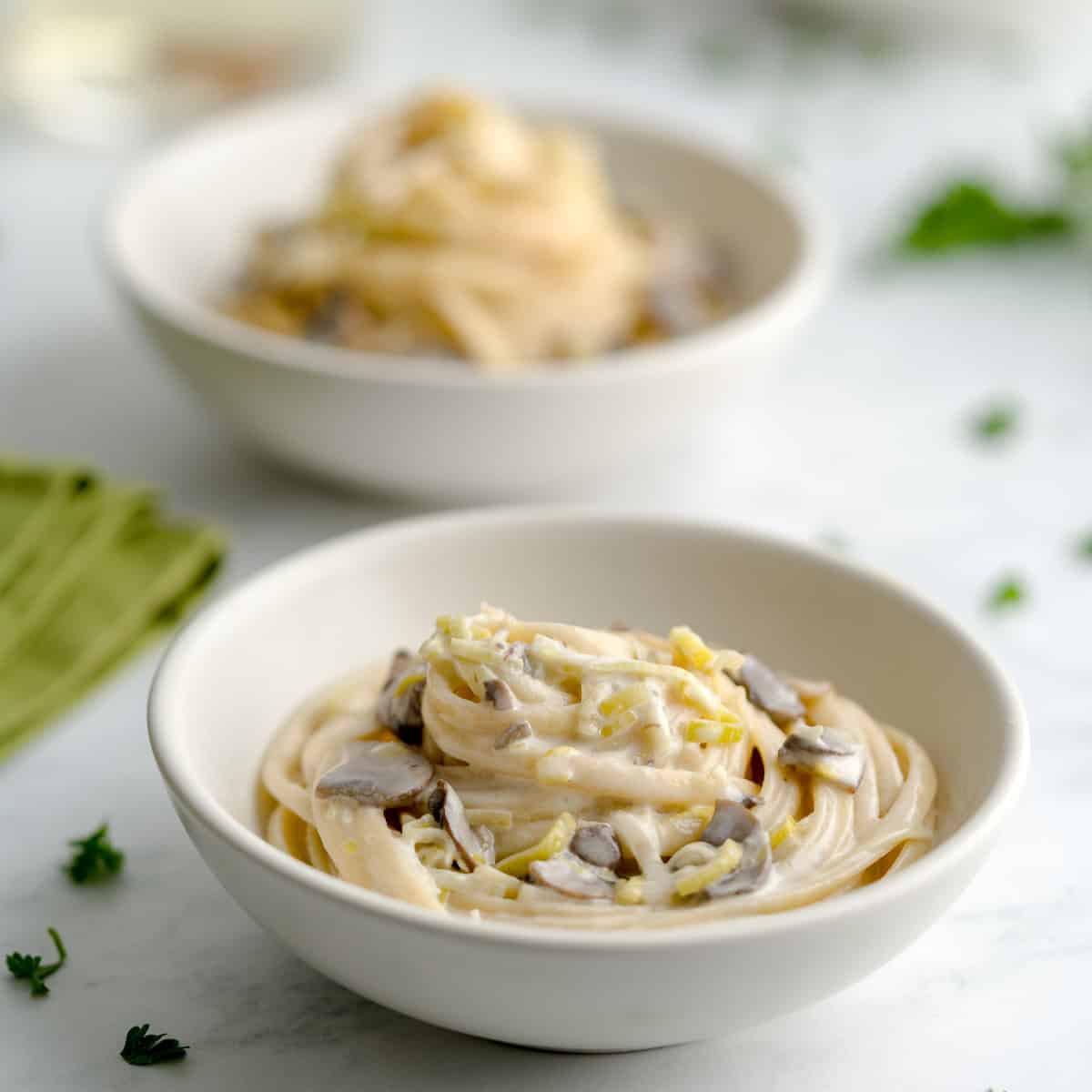 Bowl of creamy leek and mushroom pasta with fettuccine, garnished with herbs and surrounded by a sof