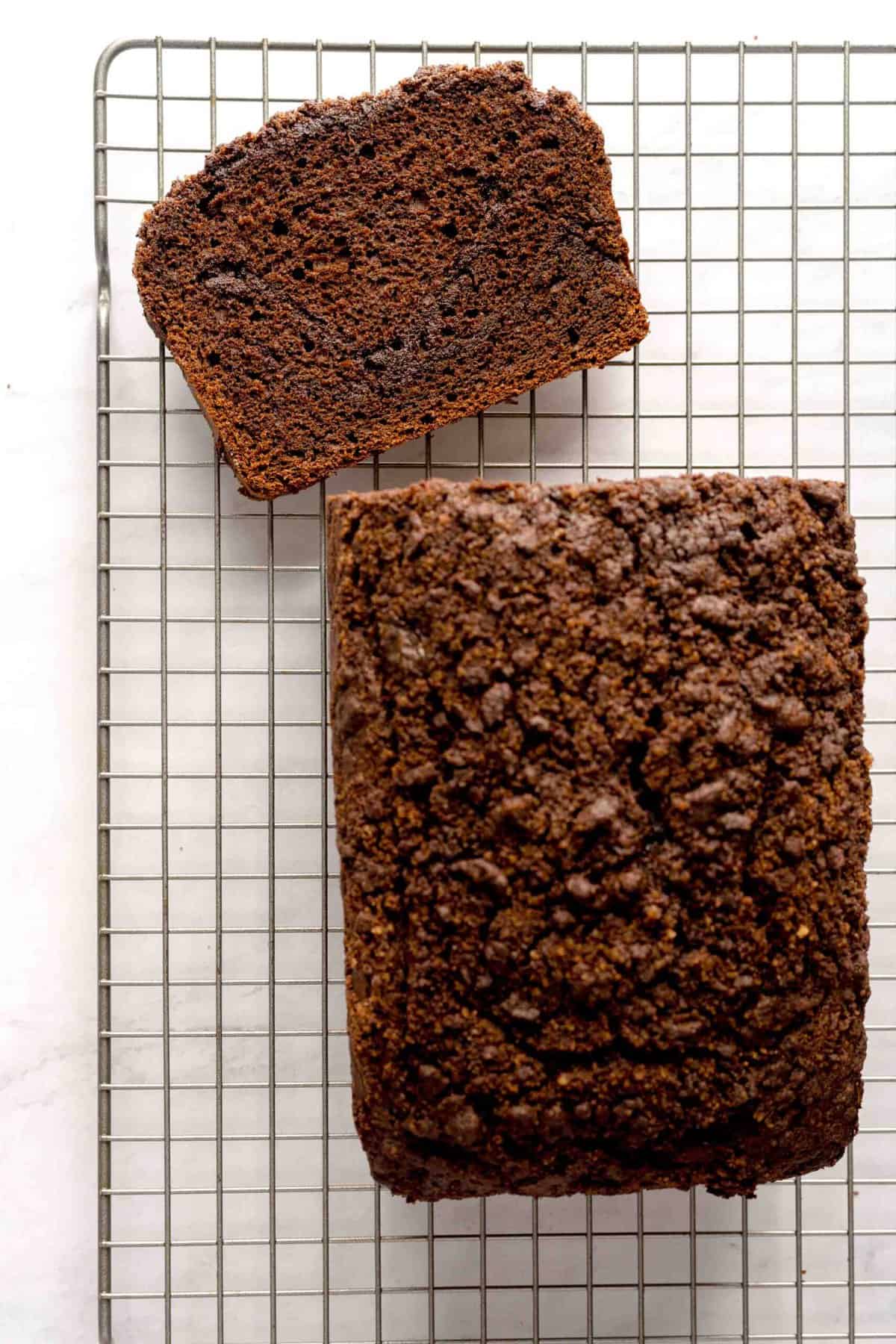 Overheard shot of a slice of chocolate espresso cinnamon loaf next to the full loaf, all on top of a wire rack.
