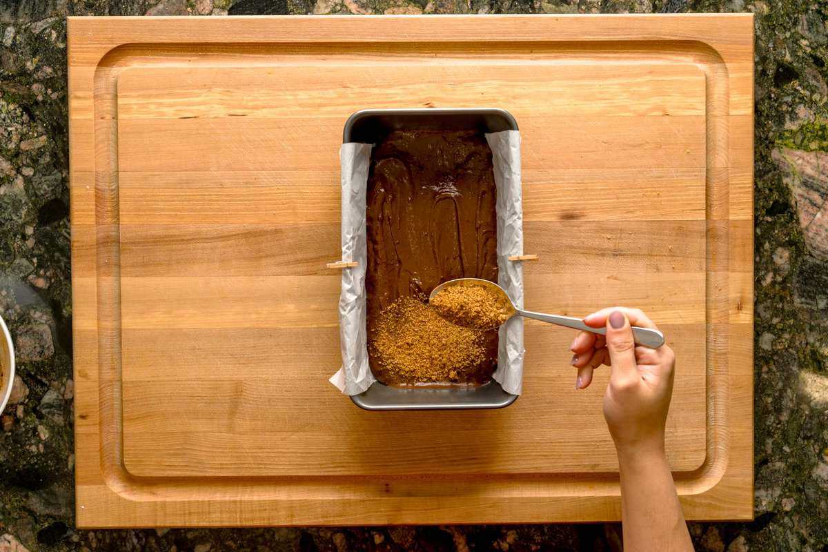 Overhead shot of a spoon sprinkling cinnamon espresso swirl on top of the prepared pan with the chocolate espresso cinnamon loaf.